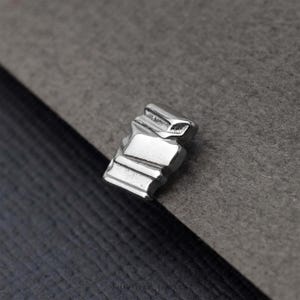 A close-up image of a small, metallic object, possibly a piece of jewelry, resting on a textured gray surface.