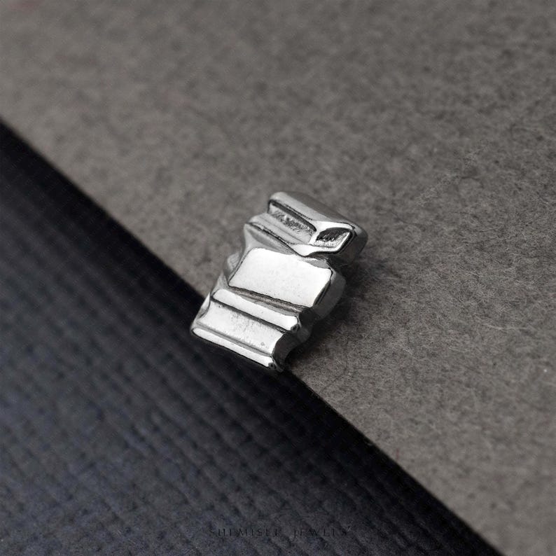 A close-up image of a small, metallic object, possibly a piece of jewelry, resting on a textured gray surface.