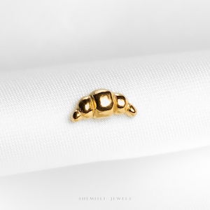 May include: A small, gold-colored croissant-shaped charm. The charm is set against a white background. The words "SHEMISLI JEWELS" are printed in white at the bottom of the image.