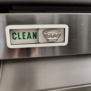 May include: A white dishwasher magnet with the word "CLEAN" in green letters and a brown outline of a bowl with wavy lines.