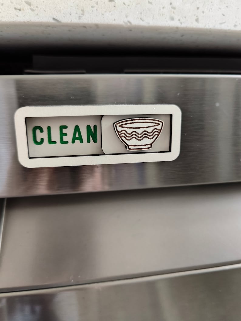 May include: A white dishwasher magnet with the word "CLEAN" in green letters and a brown outline of a bowl with wavy lines.