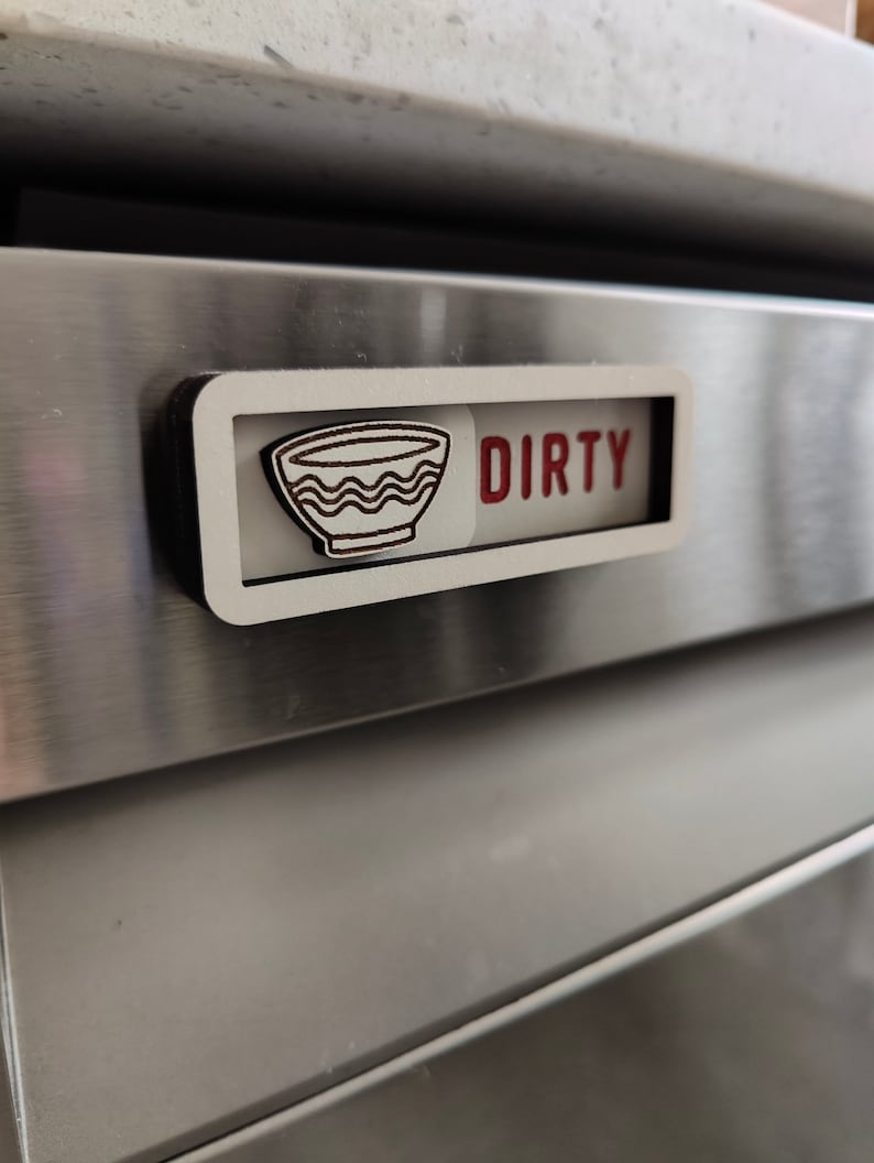 May include: A white wooden sign with the word "DIRTY" in red letters and a black and white illustration of a bowl. The sign is attached to a stainless steel appliance.