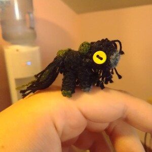 May include: A small black and green crocheted creature with a yellow button eye.