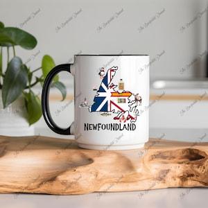 May include: White ceramic mug with a black handle and rim. The mug features a map of Newfoundland with various illustrations and the word "NEWFOUNDLAND" in black text.