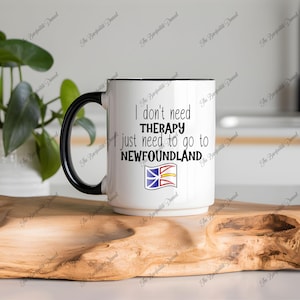 May include: White ceramic coffee mug with a black handle. The mug has black text that reads "I don't need therapy I just need to go to Newfoundland" with a small image of the Newfoundland flag.