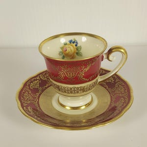 Peut inclure: Un service à thé vintage. La tasse est rouge avec des motifs dorés et une anse dorée. La soucoupe est également rouge avec des motifs dorés. L'intérieur de la tasse présente un motif floral avec une rose jaune.