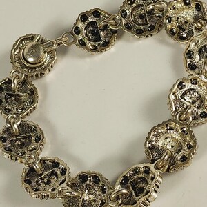 May include: Silver bracelet with flower-shaped links and black detailing. The bracelet has a secure clasp and is intricately designed. The links are connected by small chains, creating a flexible and elegant accessory. The bracelet is a stylish piece of jewellery.