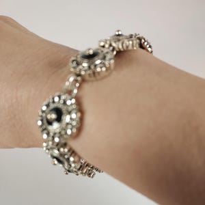 May include: Silver bracelet with a series of decorative circular links. Each link has a black centre and is surrounded by smaller, ornate details. The bracelet is displayed on a person's wrist.