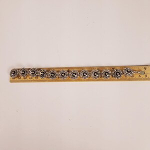 May include: Silver bracelet with circular, flower-shaped links. Each link has a dark centre and a detailed silver border. The bracelet is approximately 17.78 cm long.