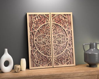 May include: Two-panel wooden wall art with intricate, layered floral and geometric designs. The artwork is in shades of light brown and reddish-brown, leaning against a dark gray wall. Decorative vases and a lantern sit on a wooden surface.
