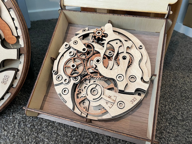 May include: A wooden model of a watch mechanism with intricate gears and a brown wooden box. The model is labelled "2901/2023" and "333".