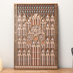 Può includere: Un'opera d'arte in legno a strati raffigurante un disegno di finestra di cattedrale. L'opera presenta dettagli intricati con sfumature di marrone, bianco e arancione. Il design include finestre ad arco, un rosone e motivi decorativi.