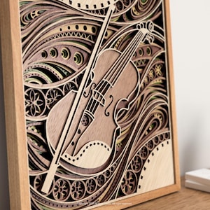 May include: A wooden layered art piece featuring a violin and bow. The artwork is framed in a light brown wooden frame. The violin and bow are light brown, with a detailed design. The background has a layered, wave-like pattern in shades of brown and green.