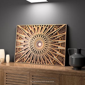 May include: A layered wooden wall art piece with a geometric sunburst design. The artwork is primarily light brown with darker brown accents, and is displayed on a wooden cabinet. A gray vase and two white vases are also on the cabinet.