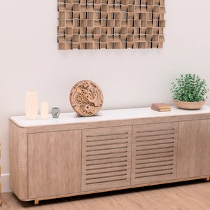May include: A wooden cabinet with a white countertop holds decorative items, including vases, a small gray cup, and a wooden clock mechanism. A gold geometric side table and a wooden wall art piece are also visible.