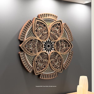 May include: A decorative wooden wall art piece with a floral design. The artwork has intricate cut-out patterns and a multi-layered construction. The colour palette includes shades of brown, beige, and black, creating a dimensional effect. It is mounted on a grey wall.