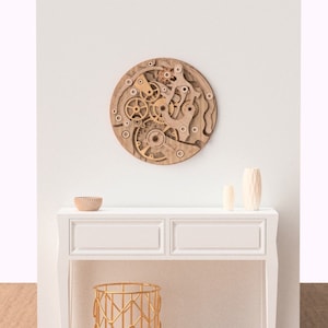 May include: A round, wooden wall art piece featuring a layered design of gears and mechanical components. The artwork is in shades of brown and beige, creating a three-dimensional effect. It hangs on a white wall above a white console table.