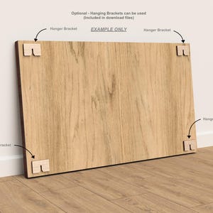 Puede incluir: Un panel de madera rectangular grande con un patr&oacute;n de vetas de madera marr&oacute;n claro. Cuatro peque&ntilde;os soportes de madera para colgar de color claro est&aacute;n unidos a las esquinas. El texto en la imagen dice "EXAMPLE ONLY" y "Hanger Bracket".