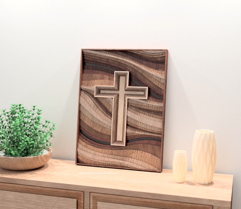 Puede incluir: Una obra de arte de cruz de madera en capas con un acabado de madera natural. La cruz es el punto focal, sobre un fondo de madera ondulada y en capas en varios tonos de marr&oacute;n. La obra de arte est&aacute; enmarcada en un borde marr&oacute;n oscuro.