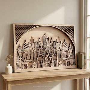 Op de afbeelding: Een houten lasergesneden kunstwerk dat een gedetailleerde stadsgezicht met ingewikkelde architectonische ontwerpen uitbeeldt. Het kunstwerk is omlijst in een rechthoekige vorm met een decoratieve boogvormige bovenkant. Het stuk is gemaakt van lichtgekleurd hout en staat op een houten tafel.