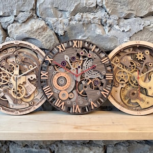May include: Three circular wall clocks featuring intricate, multi-layered wooden gear mechanisms and Roman numerals. The clocks display exposed mechanical parts in various wood tones, with the center clock featuring the text "TIME IS PRICELESS".