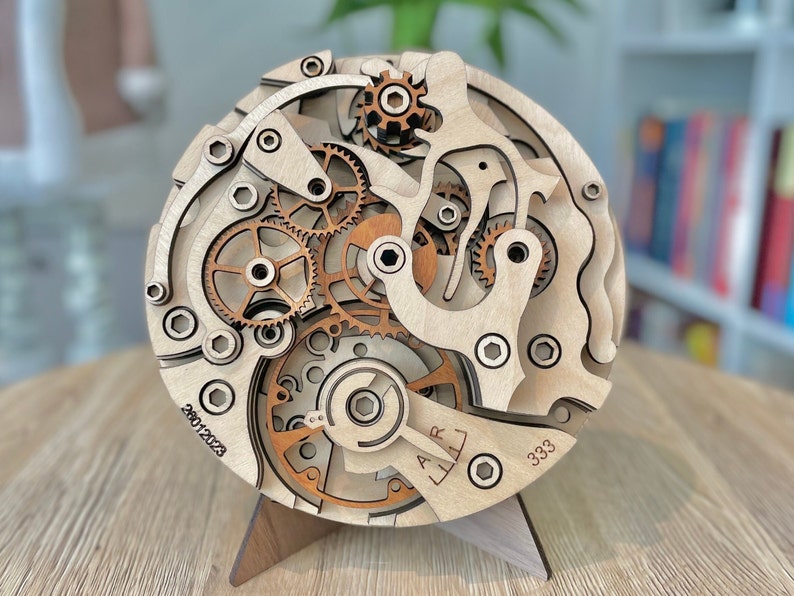 May include: A wooden, layered clock mechanism model with intricate gears and details. The model is made of light-colored wood with darker wood accents. The date 20012023 and the number 333 are visible on the face. It is displayed on a wooden stand.