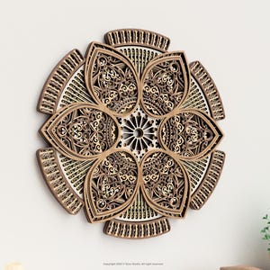 May include: A decorative wooden wall art piece in a floral design. The artwork features intricate cut-out patterns in shades of brown and beige, creating a three-dimensional effect. The piece is mounted on a white wall, with a small plant visible.