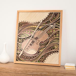 May include: A wooden layered art piece featuring a violin and bow. The artwork is framed in a light wood and showcases intricate patterns in shades of brown, green, and beige. The violin is positioned diagonally, with the bow resting across it.