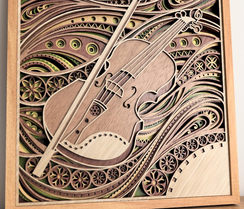 May include: A layered wooden art piece featuring a violin and bow. The artwork uses various shades of brown, green, and yellow, with intricate patterns and designs. The violin is the central focus, with the bow resting across it. The piece is framed in a light-colored wooden frame.