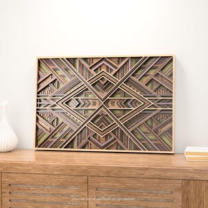 May include: Geometric wooden wall art with a layered design in shades of brown, green, and tan. The artwork is framed in a light-colored wood and features an Art Deco style. The piece is displayed on a wooden cabinet.
