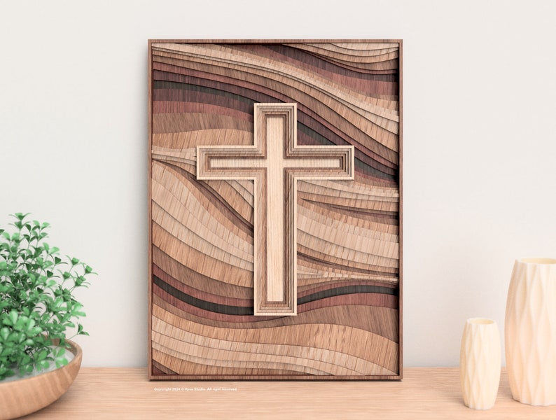 Puede incluir: Arte mural de madera con un dise&ntilde;o de cruz en capas. La cruz est&aacute; centrada sobre un fondo de madera ondulada y en capas en tonos marrones y beige. La obra de arte est&aacute; enmarcada en un borde marr&oacute;n oscuro, creando un efecto tridimensional.