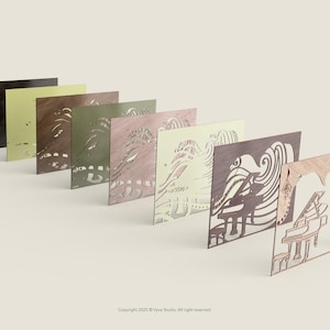 May include: A collection of laser-cut wooden art panels in various colors, including black, olive green, and light brown. The panels feature intricate designs of an eye, waves, and a piano. The panels are arranged in a row, showcasing their different colors and designs.