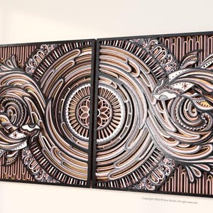 May include: Two-panel wooden wall art with intricate layered designs. The artwork features swirling patterns in shades of brown, black, white, and pink, creating a textured, dimensional effect. The design includes circular and floral motifs, framed in black.