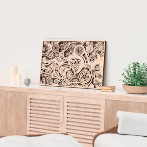 May include: A wooden wall art piece featuring a complex design of interlocking gears and mechanical elements. The artwork is displayed on a light-colored wooden cabinet, with a small plant and decorative items nearby. The overall aesthetic is modern and artistic.