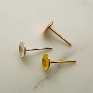 May include: Three earring posts with round metal tops. The posts are silver, gold, and rose gold.