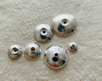May include: A set of six silver-toned metal beads with a hole in the center. The beads are different sizes and have the number "925" stamped on them.