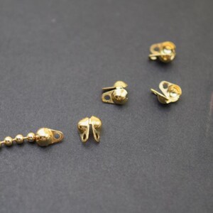 May include: Five gold metal clasps with a round ball on top. The clasps are open and ready to be attached to a chain or other jewellery.