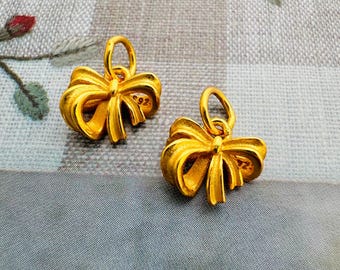 May include: Two gold-colored bow-shaped charms with a loop at the top for attaching to a necklace or bracelet.