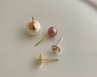May include: Three earring findings with different colored stones. One is a white pearl with a gold backing, one is a pink stone with a gold backing, and one is a clear stone with a silver backing.
