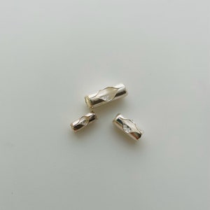 May include: Three silver metal cord ends of different sizes. The cord ends are designed to prevent fraying and are used for jewelry making.