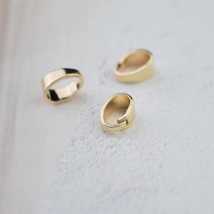 May include: Three gold-toned metal pendant clasps, each with a smooth, rounded oval shape. The clasps are designed to hold a pendant or charm.