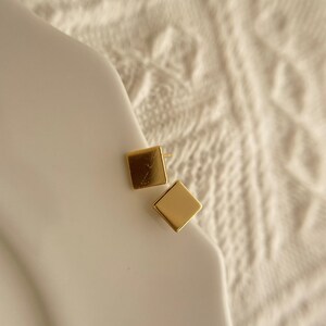 May include: A pair of gold square stud earrings. The earrings are small and simple, and they would be a great addition to any jewellery collection.