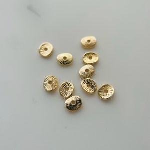 May include: A collection of ten gold-toned metal spacer beads with a textured, sunburst design. The beads have a hole in the center for stringing.