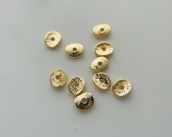 May include: A collection of ten gold-toned metal spacer beads with a textured, sunburst design. The beads have a hole in the center for stringing.