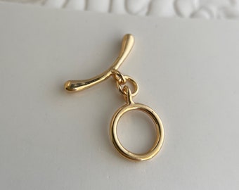May include: Gold-toned pendant with a curved bar and a circular ring. The pendant is made of metal and has a simple, modern design.
