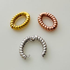 May include: Three oval-shaped jewelry clasps in gold, rose gold, and silver. The clasps have a textured, rope-like design. The silver clasp is marked with "S925". These clasps are used for jewelry making.