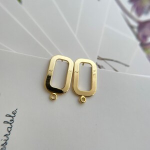 May include: A pair of gold-toned metal earring blanks with a rectangular shape and a small loop at the bottom.