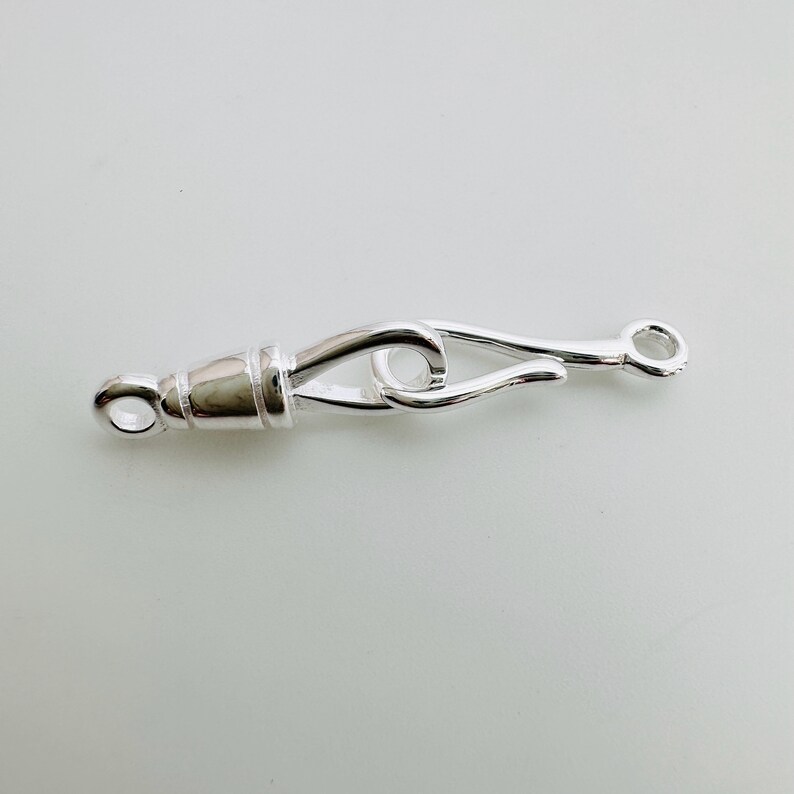 May include: Silver-toned metal clasp with a hook and loop design. The clasp is designed to be used for jewelry making or other crafting projects.