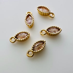 May include: Five gold-toned pendant charms with a marquise-shaped clear pink stone set in each. Each charm has a small loop for attaching to a necklace or bracelet.
