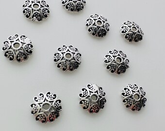 May include: Ten silver-toned metal bead caps with a decorative floral design. The caps are round and have a hole in the center.